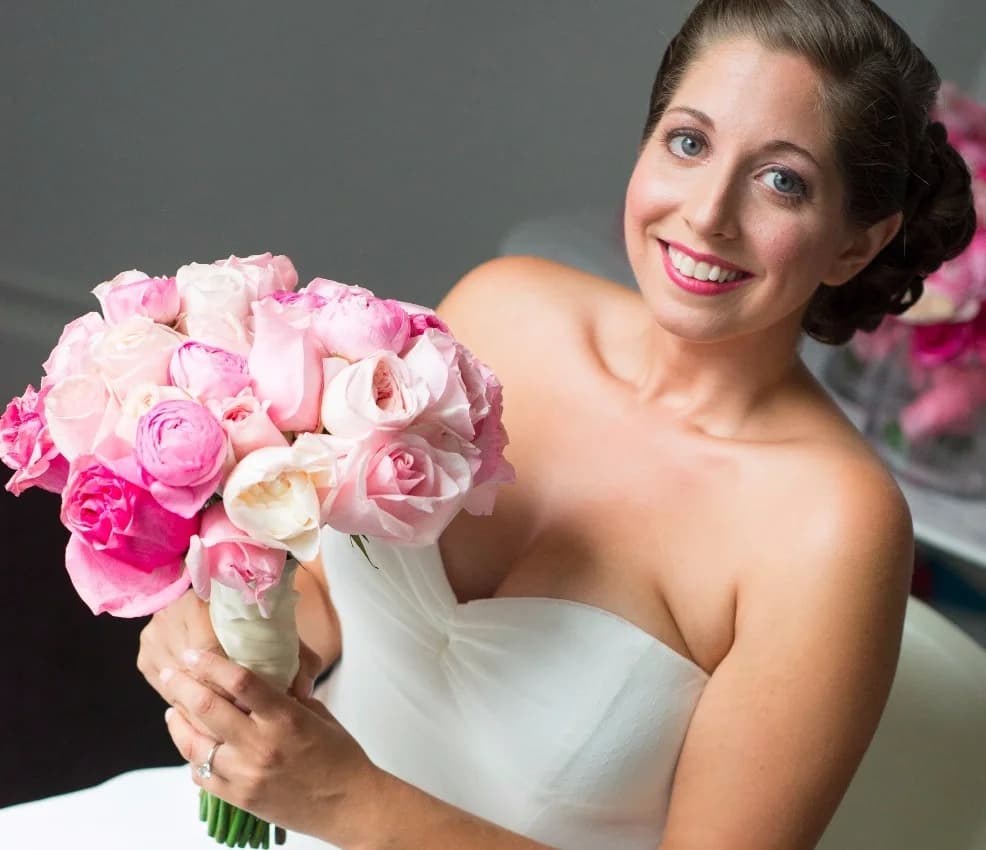 Smiling bride in a strapless gown holding pink roses