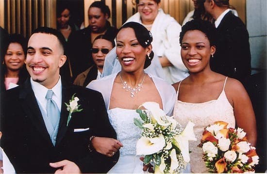 Bride and groom walking arm in arm with a bridesmaid, guests behind them